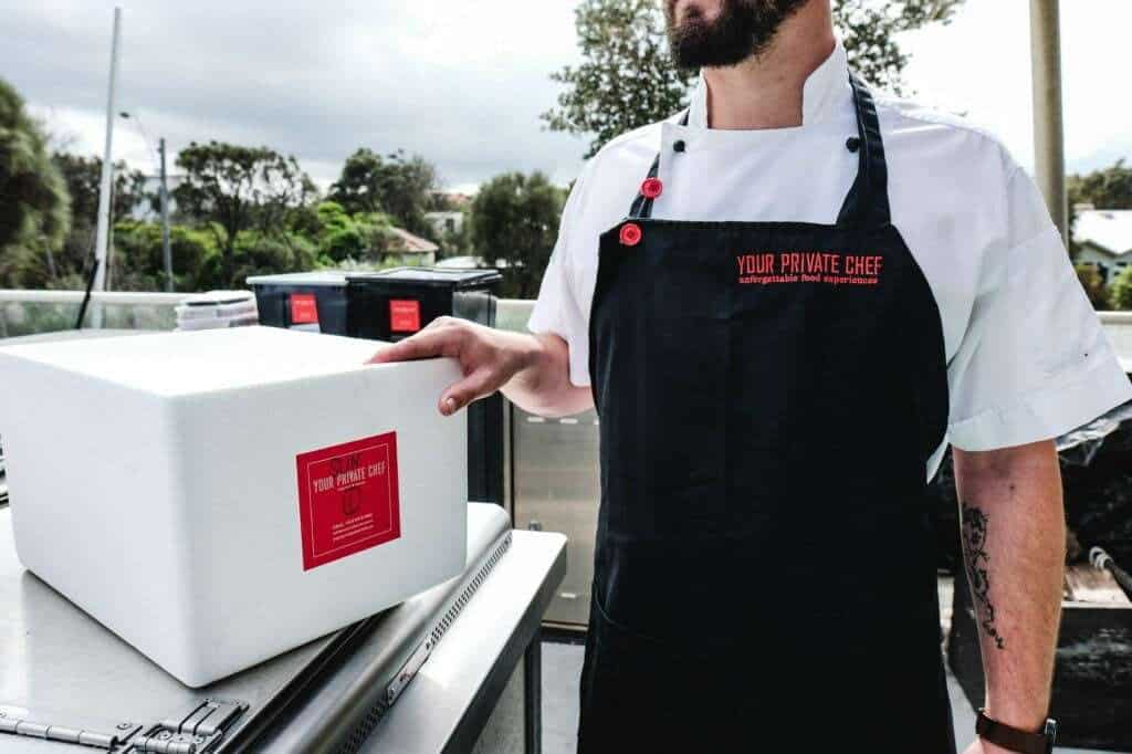 Private chef delivering gourmet meals in a cooler box on a scenic outdoor deck.